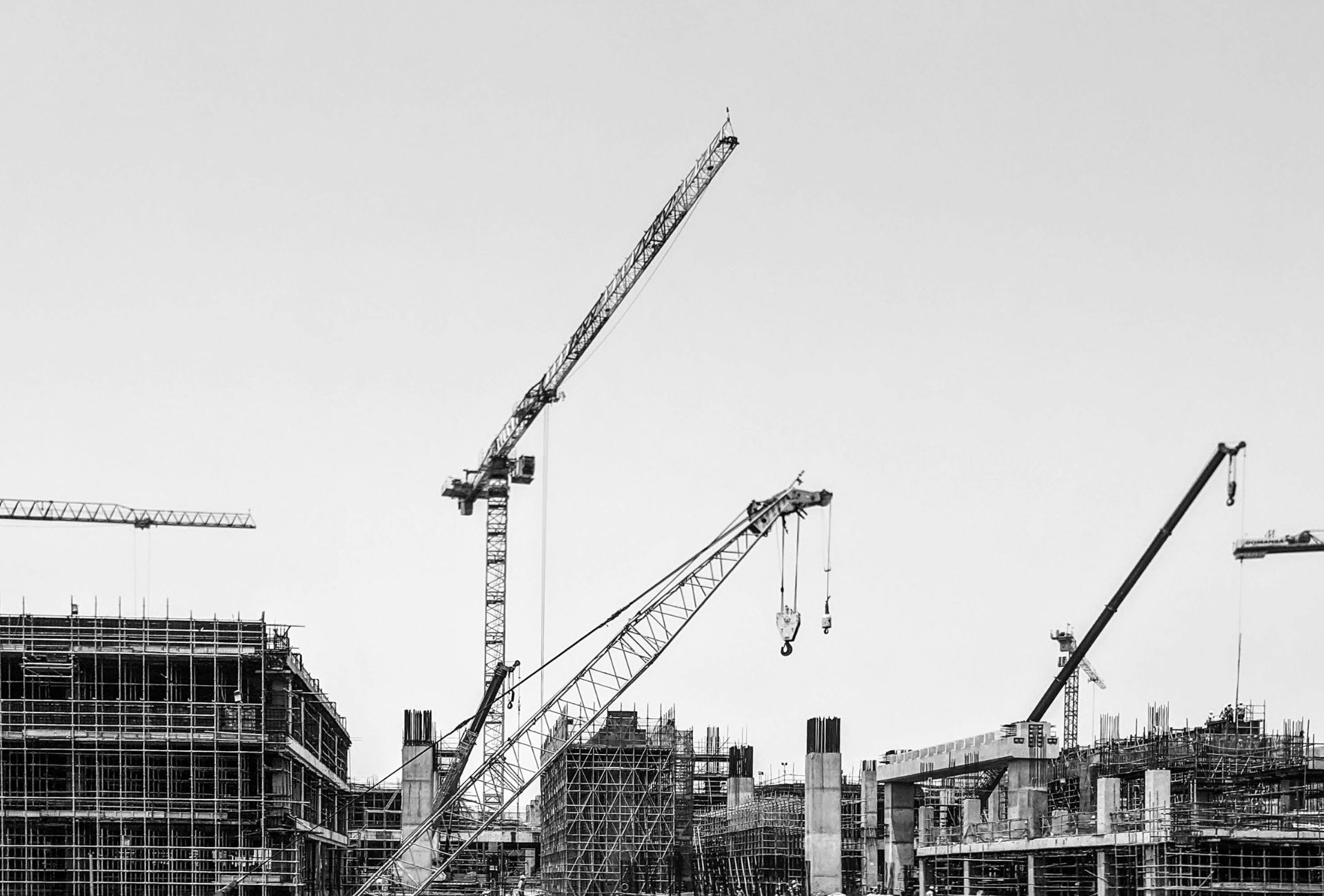 Black and white view of construction cranes against the sky
